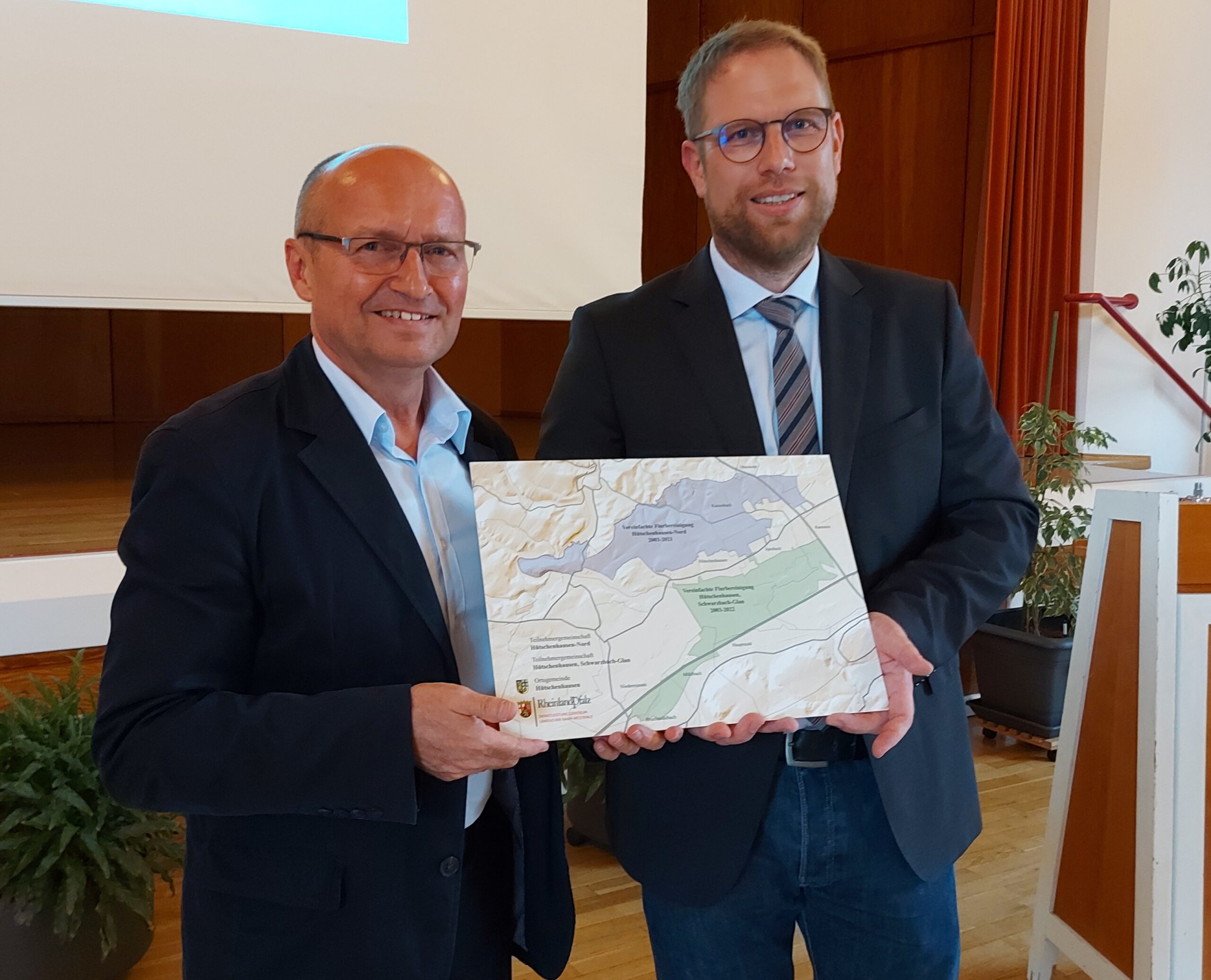 Der Dienststellenleiter des DLR Westpfalz übergibt Bürgermeister Matthias Mahl eine Metalltafel auf der die beiden Flurbereinigungsabschnitte Nord und Süd aufgebracht sind.